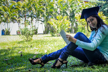 Chica sentada leyendo en el césped después de la graduación