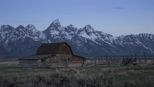 4K timelapse gentle sunrise over Grand Teton winter mountains with old historic wooden barn building on foreground. Early cold morning in National park with cinematic nature landscape, USA Wyoming 