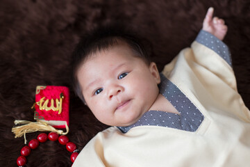 A cute Asian infant Muslim in thobe and rosary beads on red, muslim bead on bed in the home, translation is the name of muslim God "Allah" in arabic text