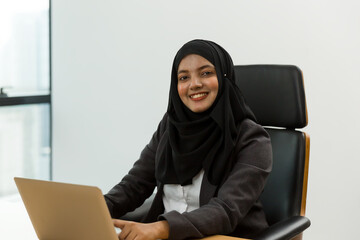 Asian Muslim woman in hijab headscarf typing computer laptop with happy and smile in the modern office. business people, diversity and office concept