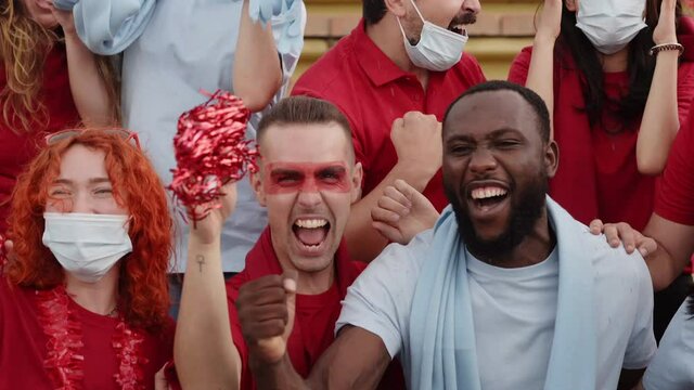 Group of people of different races follow the soccer match in the stands. Men and women celebrating a goal dressed in their team's kit.