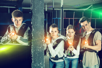 Obraz na płótnie Canvas Glad young people posing with laser guns having fun on dark lasertag arena.