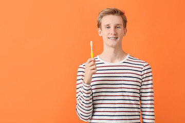 Handsome man with dental braces and toothbrush on color background