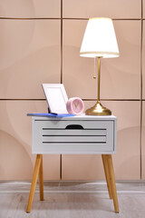 Alarm clock, lamp and photo frame on table near color wall in room