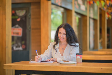 Cheerful elegant elderly woman smiling. Head shot close up portrait happy healthy middle aged woman sitting in a cafe, writes down her thoughts in a diary