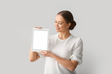 Beautiful young woman holding tablet computer with blank screen on grey background