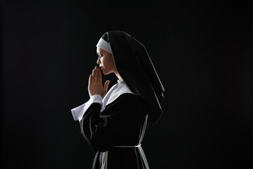 Young praying nun on dark background