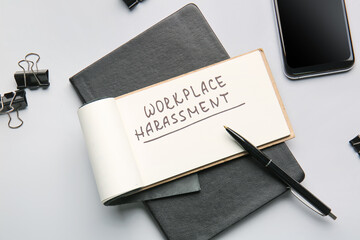 Notebook with text WORKPLACE HARASSMENT and mobile phone on light background