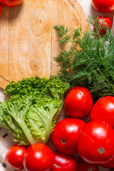 Fragment of round cutting wooden board, around lies a mountain of red tomatoes, leaves of greenery, dill.