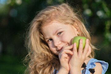 Little girl smiles at the camera. pretty girl posing for a photo and holding two green fresh apples in her hands