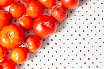 Ripe tomatoes lie on a white table with round holes.