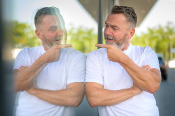 Fototapeta premium Playful man leaning against a window pointing at his reflection