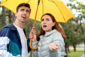 Displeased young couple with umbrella in park