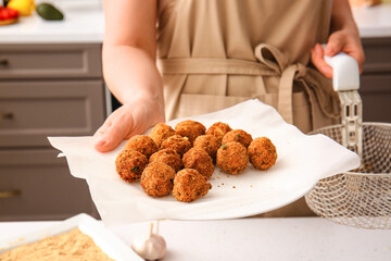 Woman holding plate with cod cutlets in kitchen, closeup