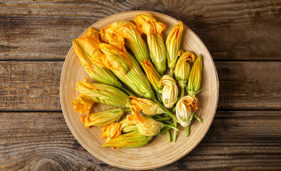 Plate with flowers of zucchini on wooden background