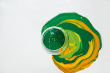 Green and yellow acrylic inks flows down in to the wineglass chemistry cocktail - 458873815