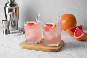 Glasses of tasty grapefruit margarita, fruits and shaker on light background