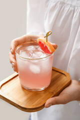 Woman holding glass of tasty grapefruit margarita on light background, closeup