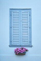 Light blue window with closed shutters and a basket of violets, Greece. Front view.
