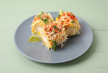 Plate with pieces of tasty Elote Mexican Street Corn on green wooden background
