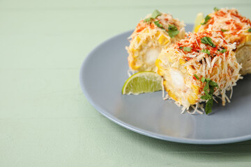 Plate with pieces of tasty Elote Mexican Street Corn on green wooden background, closeup