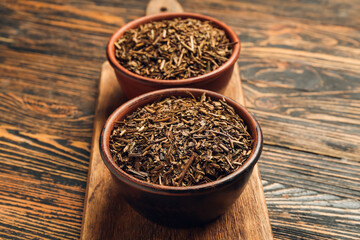 Bowls of dry hojicha green tea on wooden background