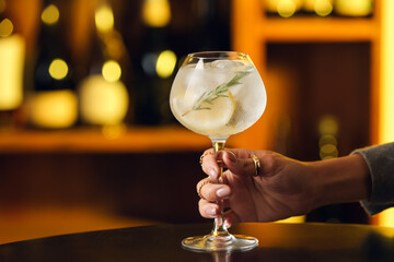 Female hand with glass of cold gin tonic on table in bar