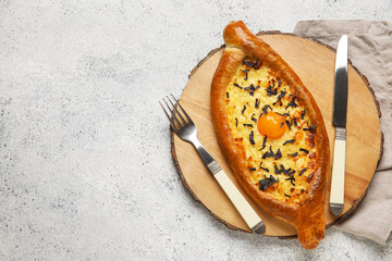 Wooden board with tasty Ajarian khachapuri on light background