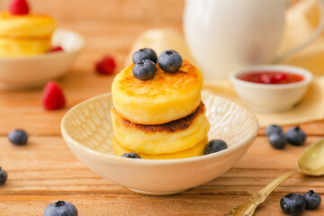Bowl with cottage cheese pancakes and blueberries on wooden background