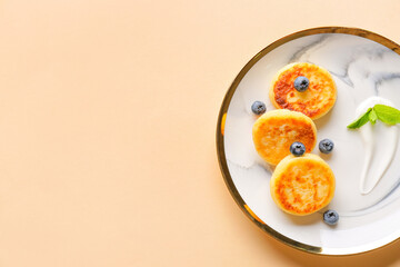 Plate with cottage cheese pancakes and blueberries on color background