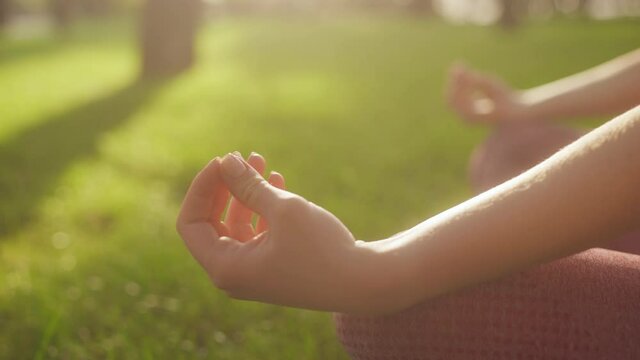 Woman sitting in lotus position, pressing fingers tightly, meditating in park