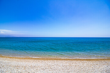 Fototapeta na wymiar Pebbles on the beach and turquoise sea against clear blue sky. Summer background