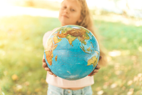 Child with Earth Globe. Portrait of a blonde European girl of elementary school with an educational globe of the planet Earth in nature in sunny weather. Study, education, conservation and