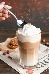 Female hand with glass of tasty latte and nuts on table