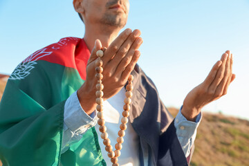 Praying Muslim man with flag of Afghanistan and tasbih outdoors