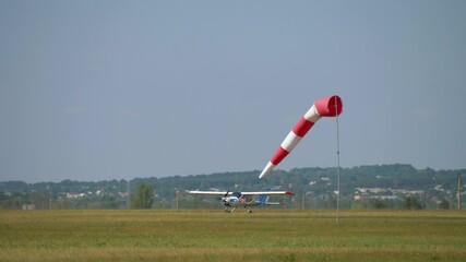 Striped windsock swings in wind on blue sky background. Red white cone airsock. Indicator of wind direction and speed. Visual signal at airport. Small plane landed on runway