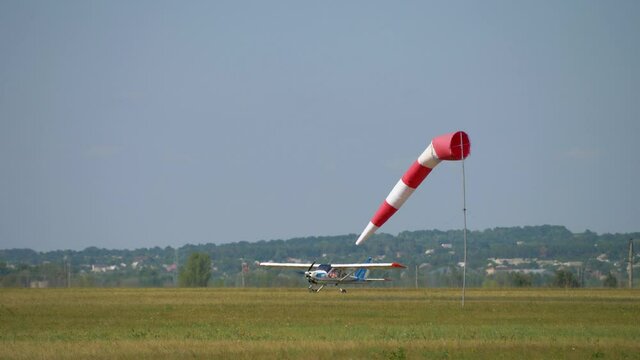 Striped windsock swings in wind on blue sky background. Red white cone airsock. Indicator of wind direction and speed. Visual signal at airport. Small plane landed on runway