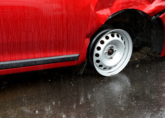 the car lost its entire tire in an accident. it has a frayed fender and a metal wheel disc stands...
