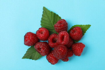 Handful of red juicy raspberries with leaves on a blue background