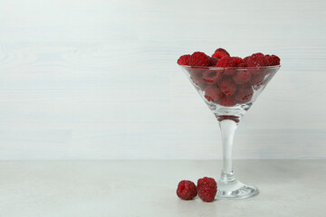Red juicy raspberries in a glass on a white wooden background