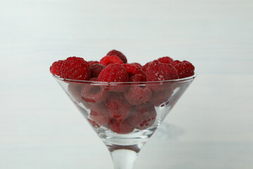 Red juicy raspberries in a glass on a white wooden background