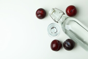 Bottle and shot of plum vodka and ingredients on white background