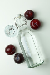 Bottle and shot of plum vodka and ingredients on white background