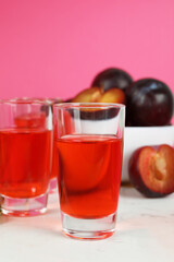 Plum brandy shots and ingredients on pink background