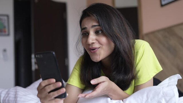 Young Indian Woman making a video call smiling and talking with her friend and family while laying on bed.Businesswoman having video call discussing,working online meeting with team at home.