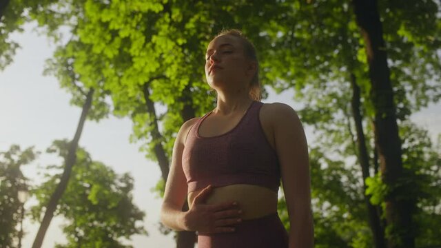 Young woman doing breathing exercises, holding hand on torso, meditation outdoor