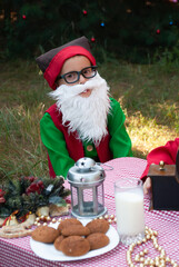 Obraz premium a little elf with a white beard sits at the Santa Claus table for the New Year and Christmas