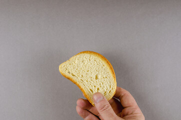 A hand holds a slice of wheat bread. An adult man and a slice of bread against a gray background. Top view.