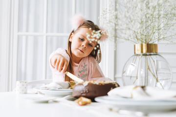 Obraz na płótnie Canvas Funny cute little girl with long hair in light pink dress with chocolate cake in hands on festive table in bright living room at the home. Christmas time, birthday girl