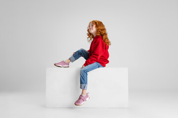 Portrait of little Caucasian red-haired curly girl dreamingly looking upward isolated over gray...
